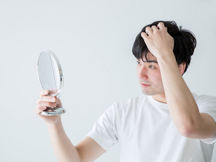 鏡を見ながら髪型を気にしている男性の画像